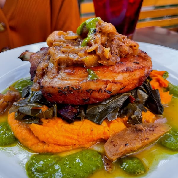 Steve's BBQ pork chop with caramelized onions, collard greens, sweet potato mash, and green sauce.