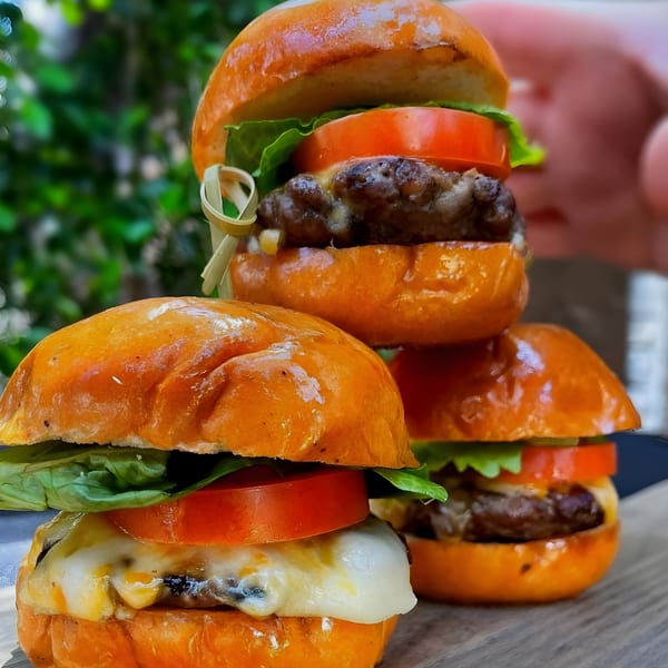 Three Steve's BBQ sliders with melted cheese, tomato, and lettuce on a wooden board.