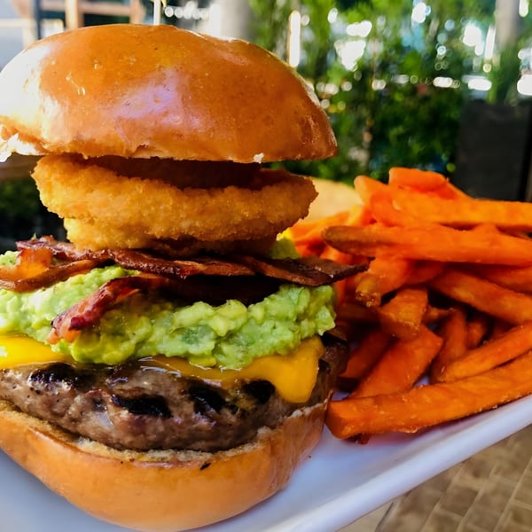 A Steve's BBQ burger with guacamole, bacon, onion rings, cheese, and sweet potato fries.