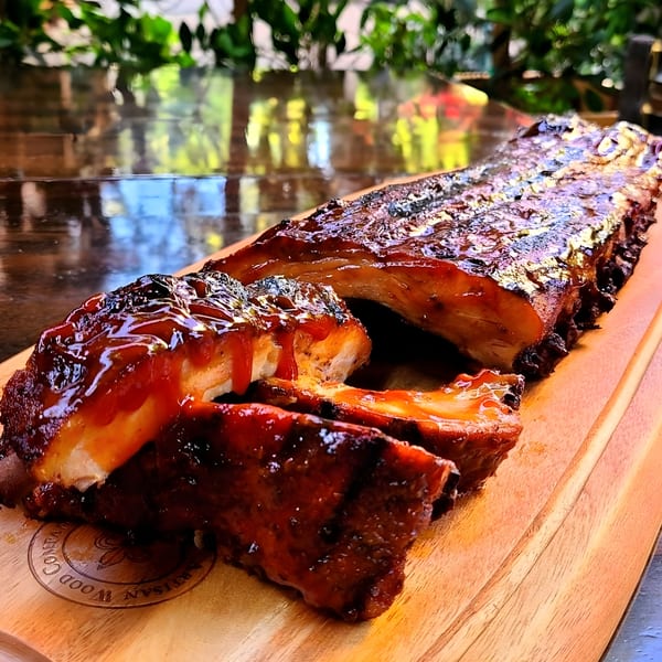 Steve's BBQ ribs, glistening with sauce, on a wooden cutting board, ready to be served.