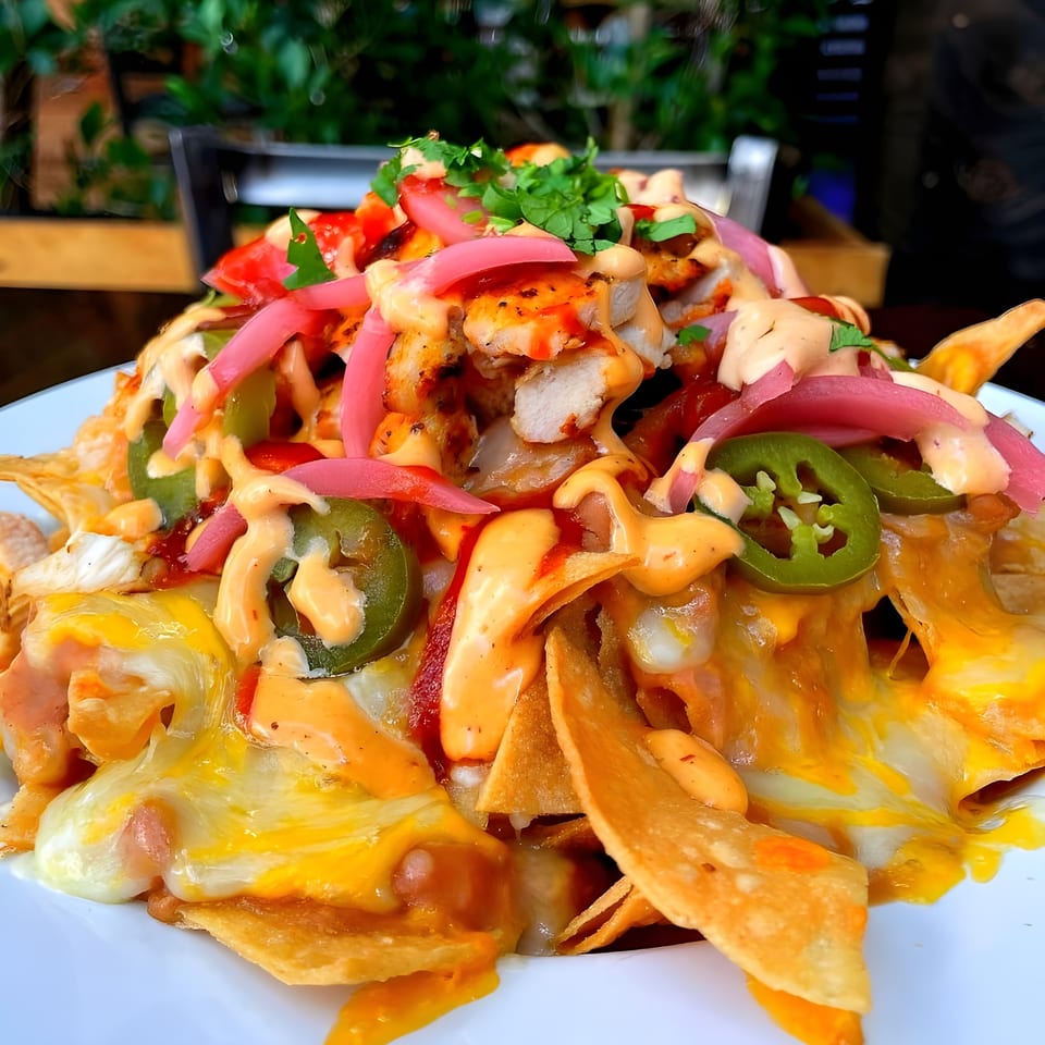 Steve's BBQ chicken nachos with melted cheese, pickled onions, jalapeños, and sauce.
